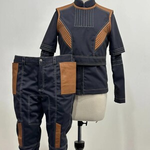 May include: A two-piece costume set featuring a navy blue jacket and matching pants. The jacket has brown accents and white stitching. The pants have brown pockets and white stitching. The costume is displayed on a mannequin.