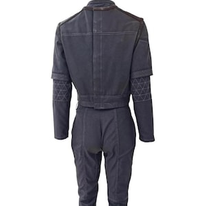May include: A dark gray jumpsuit with a cropped jacket and matching pants. The jacket features a structured design with geometric patterns on the sleeves. White stitching details the seams, and the outfit has a utilitarian aesthetic.