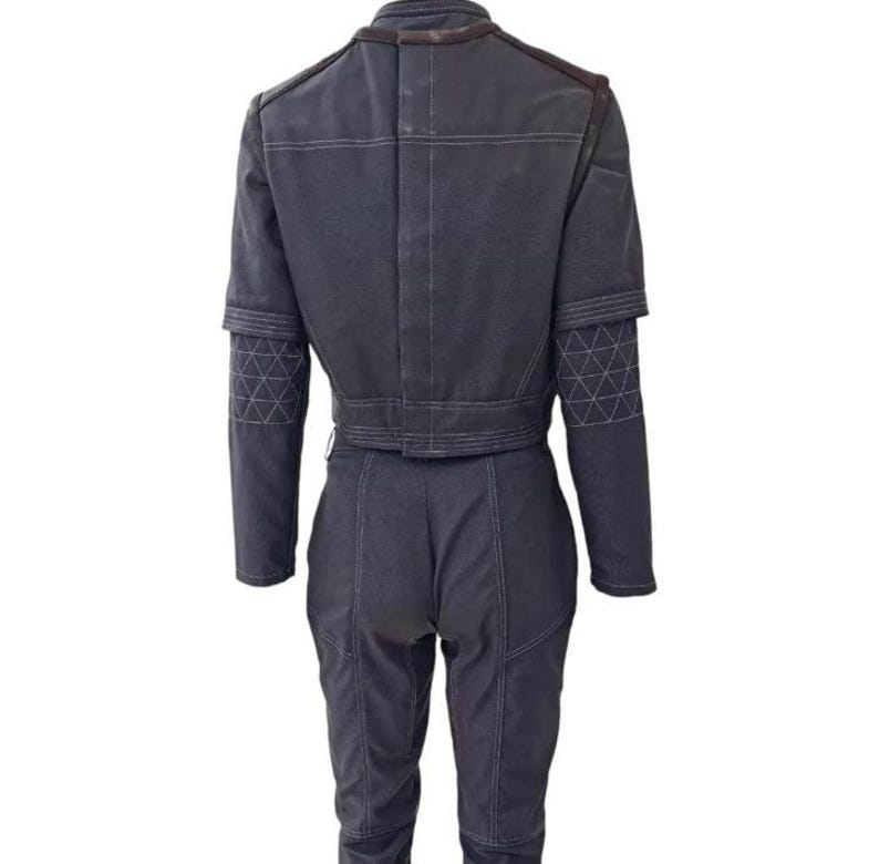 May include: A dark gray jumpsuit with a cropped jacket and matching pants. The jacket features a structured design with geometric patterns on the sleeves. White stitching details the seams, and the outfit has a utilitarian aesthetic.