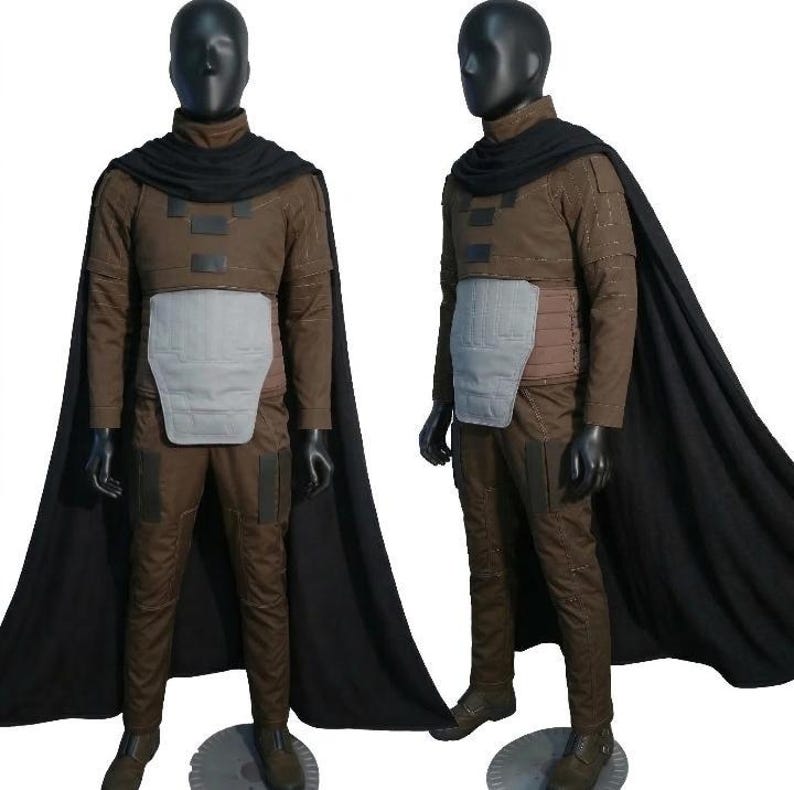 May include: A brown costume with a black cape, displayed on a mannequin. The costume includes a jacket, pants, and a chest piece. The cape drapes over the shoulders. The mannequin is wearing black gloves and boots.