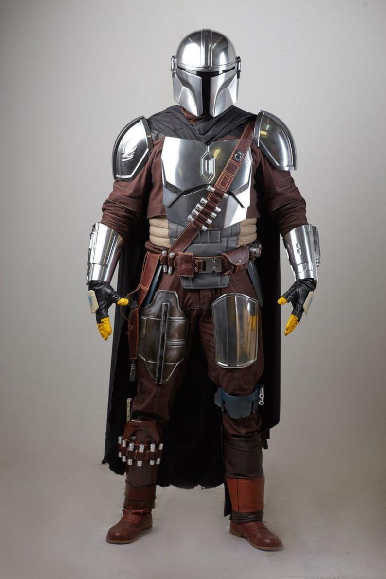 May include: Full-body shot of a detailed costume inspired by a science fiction character. The costume features a silver helmet, chest armor, and arm guards. The outfit includes brown pants, boots, and a black cape. Yellow gloves and a utility belt complete the look.