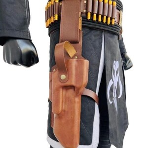 May include: A brown leather holster with a matching belt and cartridge holders. The holster is attached to a black and gray outfit with a white emblem. The belt features multiple gold-colored cylindrical objects.