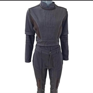 Puede incluir: Un conjunto de dos piezas en color gris oscuro. La parte superior tiene cuello alto, mangas largas y cintura entallada. Los pantalones son de cintura alta con cierre de bot&oacute;n y bolsillos. Costuras blancas detallan las costuras y paneles. Acentos de tela marr&oacute;n en hombros y rodillas.
