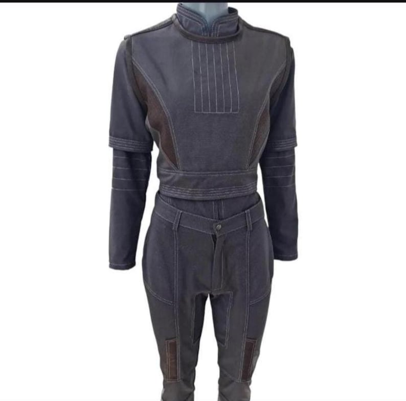 Puede incluir: Un conjunto de dos piezas en color gris oscuro. La parte superior tiene cuello alto, mangas largas y cintura entallada. Los pantalones son de cintura alta con cierre de bot&oacute;n y bolsillos. Costuras blancas detallan las costuras y paneles. Acentos de tela marr&oacute;n en hombros y rodillas.