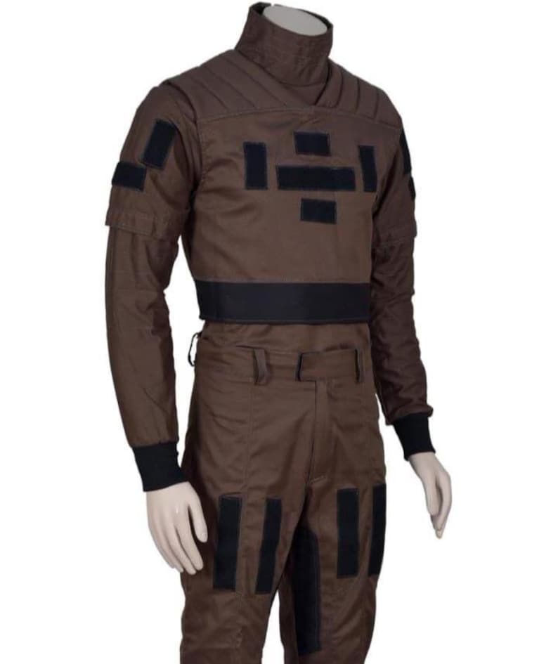 May include: Brown jumpsuit with black accents, featuring a high collar and multiple rectangular patches. The long-sleeved top has a black band at the waist and cuffs. The pants have black rectangular patches down the legs. The outfit is displayed on a mannequin.
