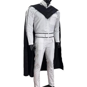May include: A white jumpsuit with black trim and a matching black cape. The outfit features a high collar, a zip-up front, and a belt. The mannequin is wearing black shoes. The outfit is displayed on a mannequin.