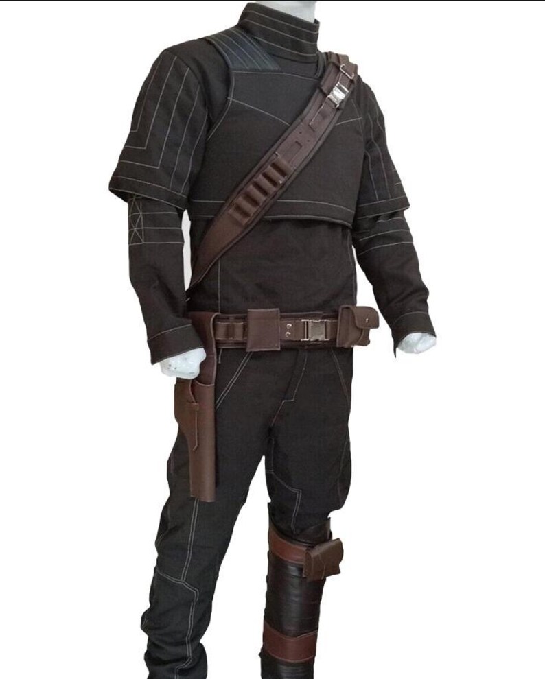 K&ouml;nnte beinhalten: Ein dunkelbraunes Kost&uuml;m mit hohem Kragen, Schulterpolstern und einem braunen Lederriemen &uuml;ber der Brust. Das Kost&uuml;m umfasst eine passende Hose, einen G&uuml;rtel mit Taschen und eine Halterung. Das Outfit hat wei&szlig;e Nahtdetails.