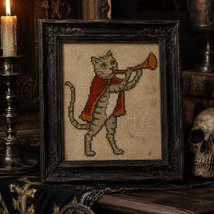 May include: A cross-stitch embroidery of a cat wearing a red cape and playing a trumpet, displayed in a dark, ornate wooden frame. The cat is depicted in profile on a beige fabric background, featuring detailed stitching in shades of gray and red.