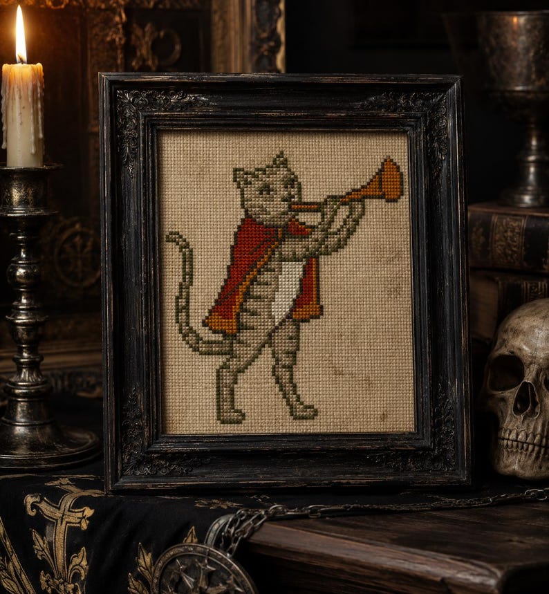 May include: A cross-stitch embroidery of a cat wearing a red cape and playing a trumpet, displayed in a dark, ornate wooden frame. The cat is depicted in profile on a beige fabric background, featuring detailed stitching in shades of gray and red.