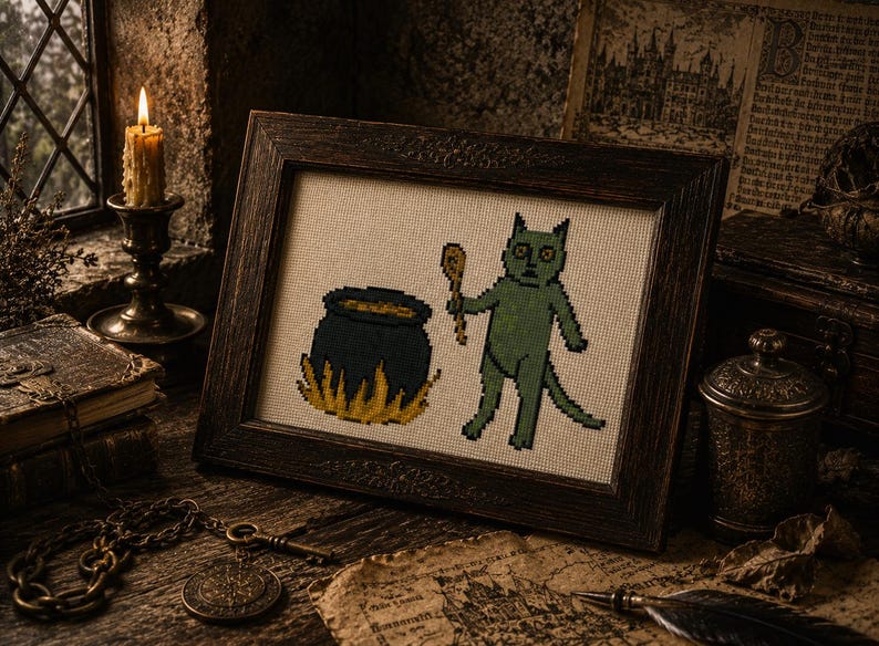 May include: A framed cross-stitch embroidery featuring a green cat-like creature holding a wooden spoon next to a dark blue cauldron with yellow flames at the base, all set against a light-colored fabric background within a dark wooden frame.