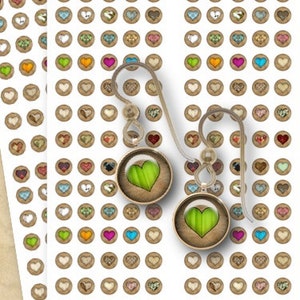 May include: Two pairs of dangle earrings with green heart-shaped glass charms. The earrings are on a sheet of paper with multiple small heart-shaped stickers.