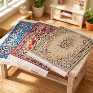 Puede incluir: Tres alfombras rectangulares en miniatura con intrincados patrones florales y geométricos, con bordes de flecos en los lados cortos. Las alfombras son de tonos azul, rojo y beige, cada una con un diseño de medallón central.
