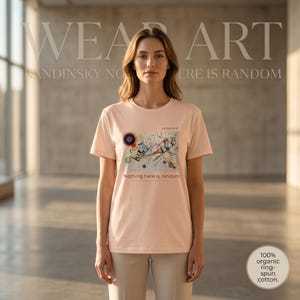 以下が含まれることがあります： 淡いピーチカラーの半袖Tシャツ。抽象的な幾何学模様の絵画が長方形のグラフィックとしてプリントされています。胸元には「MODERNIST」および「Nothing here is random」という小さな黒い文字が中央に配置されています。
