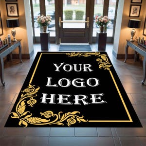 May include: Black rectangular welcome mat with gold trim and floral corner designs. The mat features the text "YOUR LOGO HERE" in white, centered on the black background. The mat is placed in a doorway.