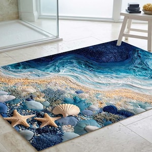 Pode incluir: Um tapete de banho retangular com uma cena de praia com um oceano azul, praia arenosa e conchas. O tapete inclui estrelas do mar, seixos e um desenho de ondas. A paleta de cores inclui tons de azul, bege e castanho.