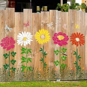 May include: A wooden fence decorated with colorful floral decals featuring a pink peony, a white daisy, a yellow sunflower, a magenta peony, and an orange gerbera daisy, all with green stems and leaves, accented by small butterfly and insect stickers.