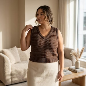 Peut inclure: Une femme porte un gilet sans manches marron à col en V. Le gilet présente un motif texturé et une bordure côtelée. Elle porte une jupe crème. L'arrière-plan comprend un canapé, une table et une fenêtre avec de la lumière naturelle.