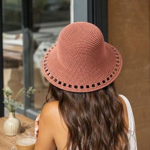 Peut inclure: Un chapeau bob en crochet de couleur terre cuite, doté d'une calotte en mailles serrées et d'un large bord. Le bord est orné d'un motif répétitif de découpes rectangulaires disposées en une seule rangée sur toute la circonférence.