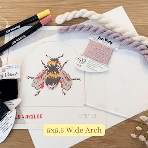 May include: A needlepoint kit featuring a bee design on a white canvas. The kit includes various colored threads, markers, and the text "5x5.5 Wide Arch". The color palette includes yellow, pink, black, and cream.