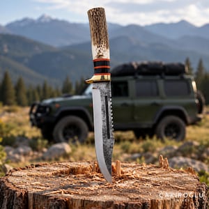 Puede incluir: Un cuchillo de hoja fija con mango de asta texturizada, guarda de latón y dos espaciadores negros y naranjas. La hoja presenta un acabado oscuro y martillado con el lomo dentado y un filo liso. El texto ÇAKIROĞLU KNIVES es visible.