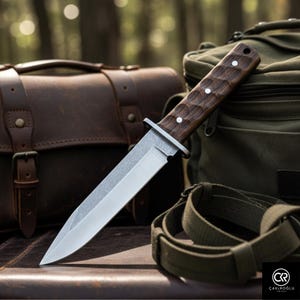 Peut inclure: Couteau en acier inoxydable avec un manche en bois foncé et trois rivets blancs. Le couteau est placé devant une sacoche en cuir marron, un sac en toile vert et une sangle verte, évoquant un thème de survie ou d'extérieur.