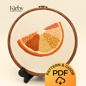 May include: Embroidered orange slice in a wooden hoop. The artwork features various shades of orange and yellow thread, creating a textured effect. The text "Kirby Embroidery" is at the top left. A PDF pattern and guide are also available.