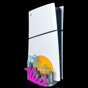 May include: A white video game console featuring a decorative attachment at the base. The attachment displays a bright orange sun, two blue palm tree outlines, a grey cityscape, and the word Vice in a vibrant pink script font.