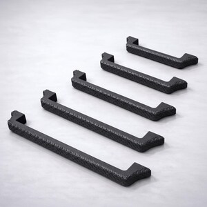 May include: A set of five matte black cabinet handles arranged in a diagonal row. Each handle features a rectangular bar design with a textured, diamond-patterned surface along the front and angled ends that extend outward to form mounting points.