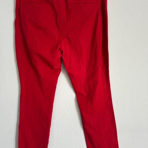 May include: Bright red, tailored pants hanging on a black hanger. The pants have a classic design with a straight leg and a back pocket. The fabric appears to be a smooth, woven material.