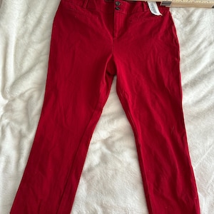 May include: Bright red pants with a button closure and a zipper. The pants are made of a solid fabric and have a classic, tailored design. A measuring tape is placed across the top of the pants.