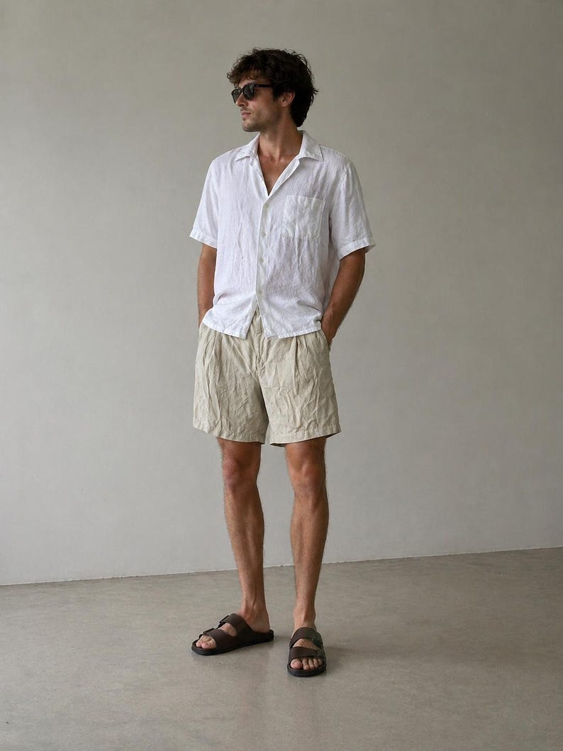 May include: A person wearing a white short-sleeved shirt, beige shorts, and brown sandals. The shirt has a single pocket on the chest. The shorts are pleated. The sandals have two straps.