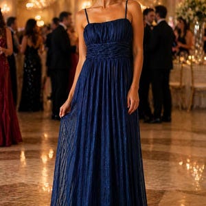 Peut inclure: Une robe de soir&eacute;e bleu marine avec de fines bretelles et un corsage pliss&eacute;. La robe longue pr&eacute;sente une taille cintr&eacute;e et une jupe fluide. Le tissu a un &eacute;clat subtil, et la robe est port&eacute;e lors d'un &eacute;v&eacute;nement formel.