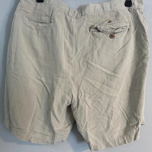 May include: Beige shorts with a buttoned back pocket and two front pockets. The shorts are made of a lightweight fabric and have a relaxed fit. The shorts are hanging on a black hanger.