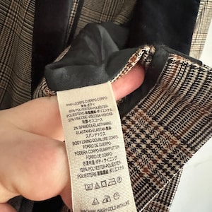 May include: Close-up of a plaid blazer interior with a black velvet collar. The fabric tag shows the material composition: 65% polyester, 33% viscose, and 2% spandex. The tag also includes washing instructions.