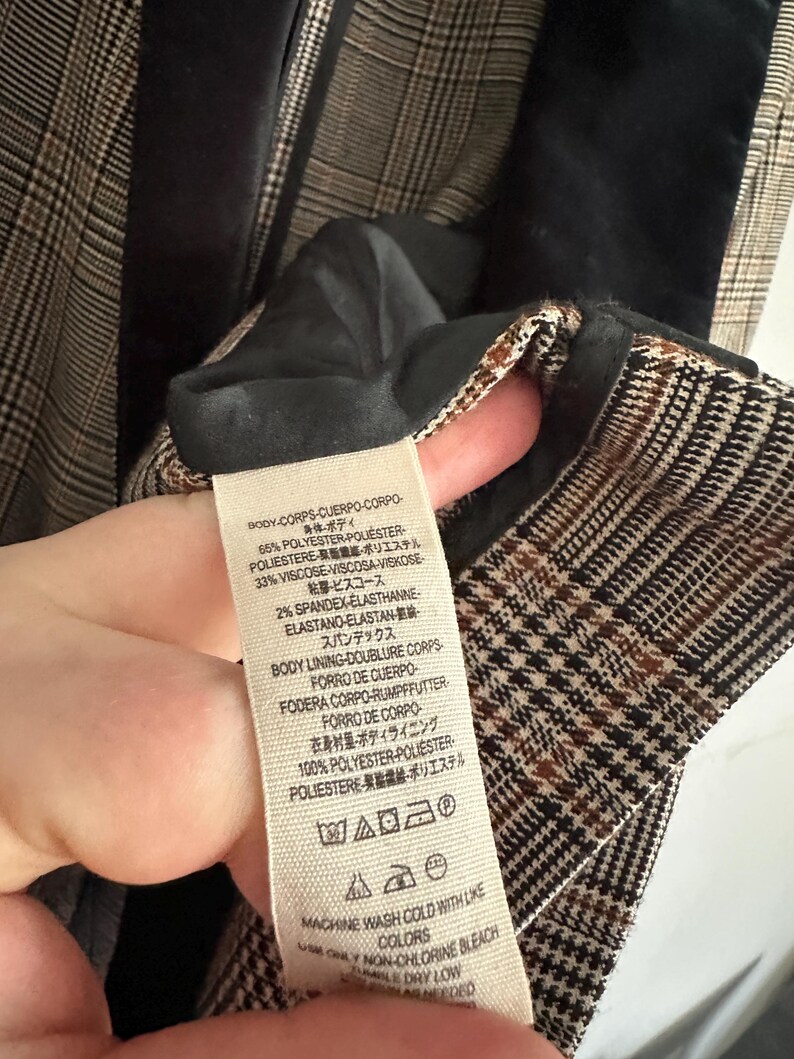 May include: Close-up of a plaid blazer interior with a black velvet collar. The fabric tag shows the material composition: 65% polyester, 33% viscose, and 2% spandex. The tag also includes washing instructions.
