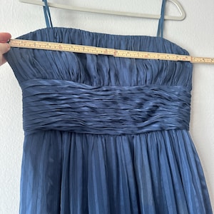 Peut inclure: Robe bleu marine &agrave; fines bretelles, suspendue &agrave; un cintre. La robe pr&eacute;sente un corsage pliss&eacute; et une jupe pliss&eacute;e. Un m&egrave;tre ruban indique que la robe mesure environ 46 cm de large au niveau de la poitrine.