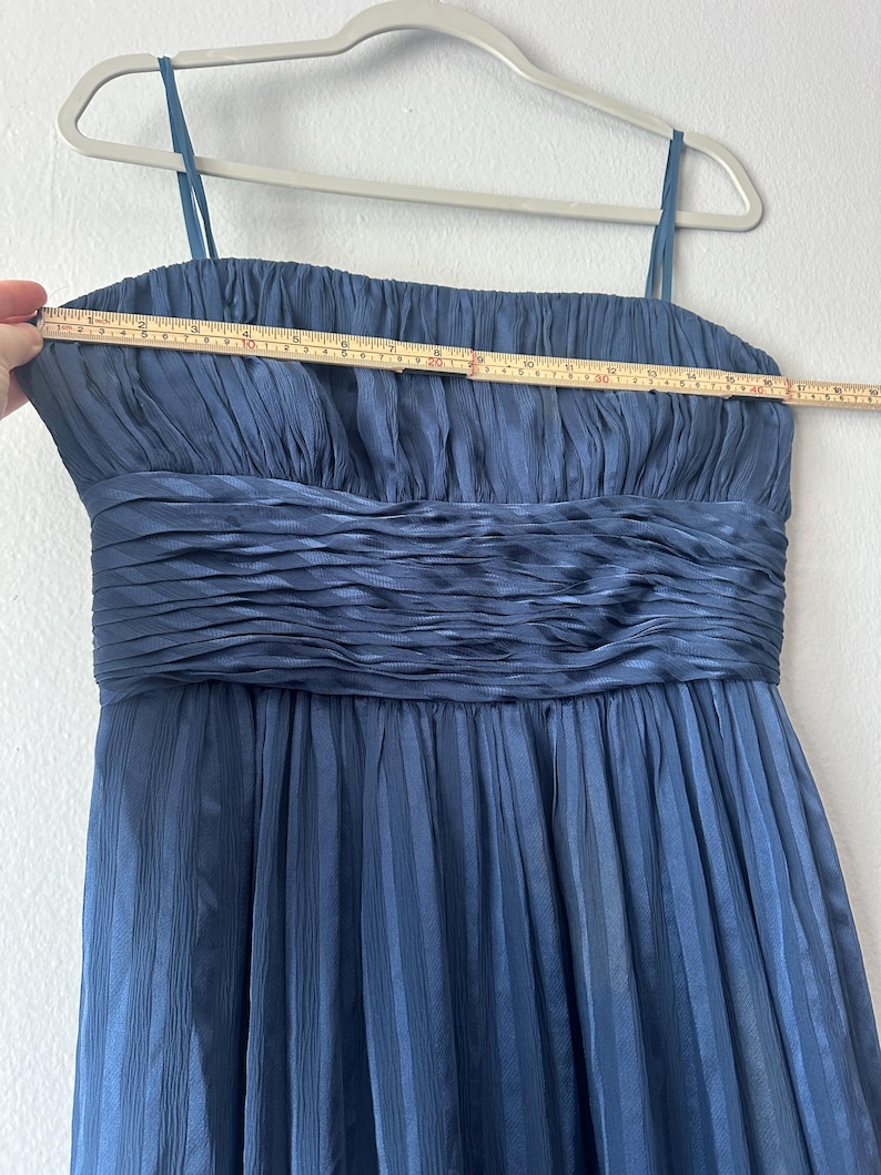 Peut inclure: Robe bleu marine &agrave; fines bretelles, suspendue &agrave; un cintre. La robe pr&eacute;sente un corsage pliss&eacute; et une jupe pliss&eacute;e. Un m&egrave;tre ruban indique que la robe mesure environ 46 cm de large au niveau de la poitrine.