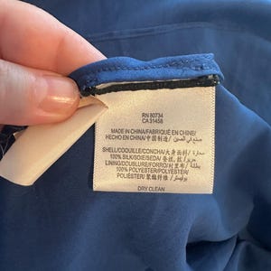 Peut inclure: Gros plan sur une &eacute;tiquette attach&eacute;e &agrave; un v&ecirc;tement bleu. L'&eacute;tiquette indique "RN 80734 CA31458 MADE IN CHINA" et d&eacute;taille la composition du tissu, dont 100% soie et 100% polyester. L'&eacute;tiquette indique &eacute;galement "DRY CLEAN".