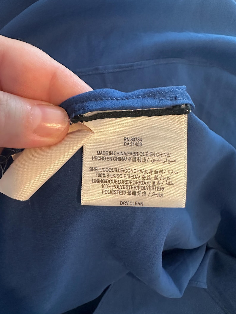 Peut inclure: Gros plan sur une &eacute;tiquette attach&eacute;e &agrave; un v&ecirc;tement bleu. L'&eacute;tiquette indique "RN 80734 CA31458 MADE IN CHINA" et d&eacute;taille la composition du tissu, dont 100% soie et 100% polyester. L'&eacute;tiquette indique &eacute;galement "DRY CLEAN".