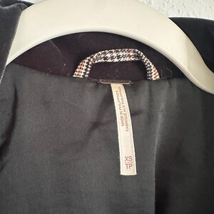 May include: Close-up of a dark gray velvet jacket hanging on a white hanger. The jacket's interior lining is black, with a brown and white patterned collar detail. A tag reads "MADE IN PHILIPPINES" and "XS TP".