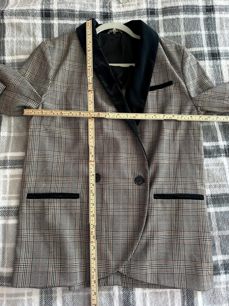 May include: A plaid blazer with a black velvet collar and pocket trim. The blazer has a double-breasted design with two buttons and two front pockets. The blazer measures approximately 30 inches in length.