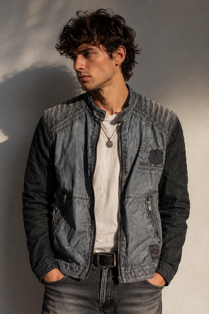 K&ouml;nnte beinhalten: Jeansjacke in verwaschenem Blau und Schwarz mit Rei&szlig;verschluss und kleinem Aufn&auml;her mit Text. Die Jacke hat ein geripptes Design an den Schultern. Das Model tr&auml;gt ein wei&szlig;es T-Shirt und eine silberne Halskette.