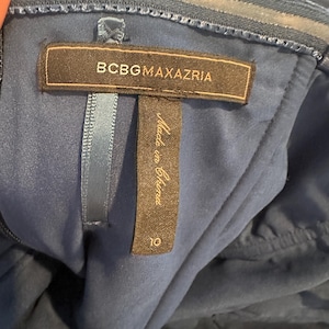 Peut inclure: Gros plan d'une robe bleu marine avec une &eacute;tiquette "BCBGMAXAZRIA". L'&eacute;tiquette indique &eacute;galement "Made in China" et une taille 10. La robe a un tissu textur&eacute; et un design sans bretelles.