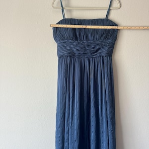 Peut inclure: Une robe de soir&eacute;e bleu marine &agrave; fines bretelles, suspendue &agrave; un cintre blanc. La robe pr&eacute;sente un corsage fronc&eacute; et une jupe fluide &agrave; rayures verticales. Une r&egrave;gle en bois est plac&eacute;e sur le corsage, mesurant environ 76 cm.
