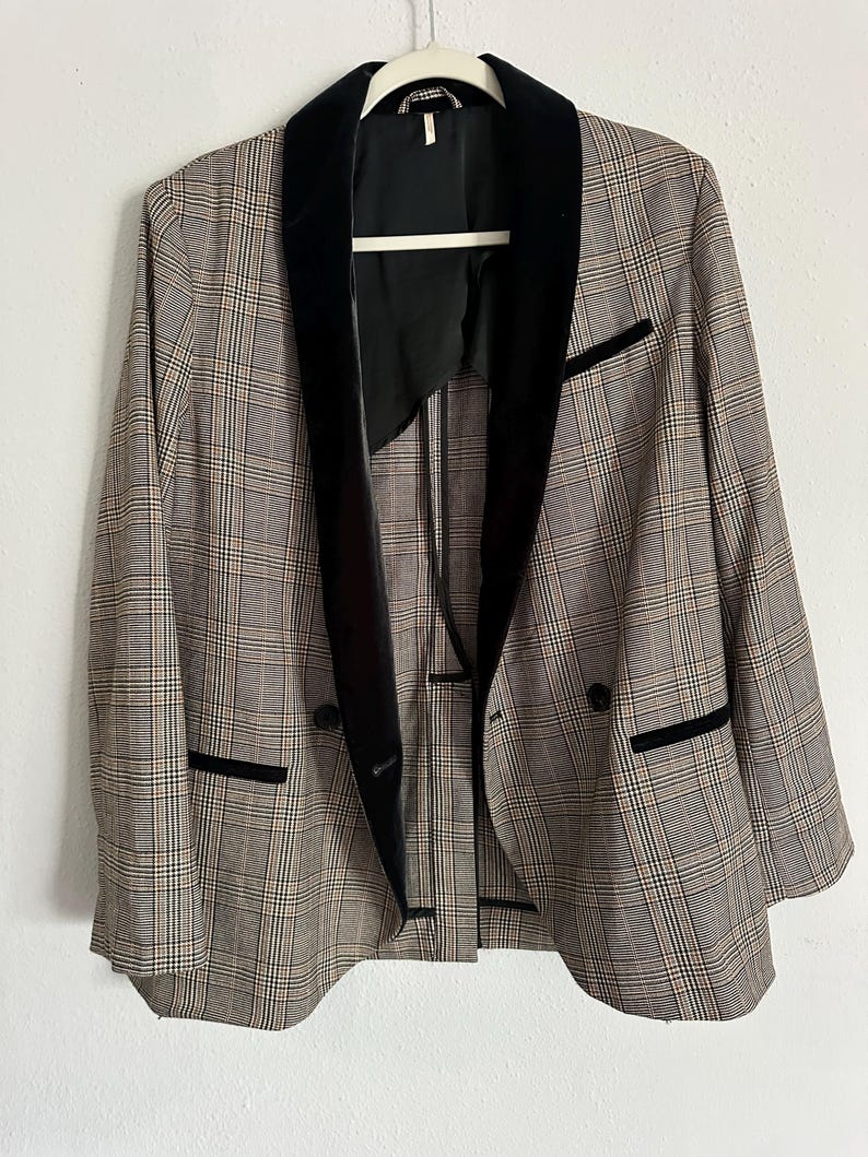 May include: A plaid blazer with a black velvet collar and trim. The jacket has a double-breasted design with two black buttons and two front pockets. The blazer is hanging on a white hanger against a white background.