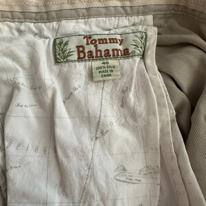 May include: Close-up of the interior of khaki-coloured Tommy Bahama trousers. The lining features a map design. The tag reads "Tommy Bahama" and "100% Silk". The waistband has the words "Tommy Bahama" and "Relax".