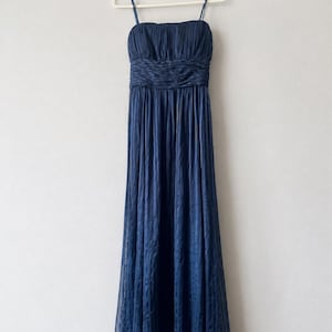 Peut inclure: Une robe de soir&eacute;e bleu marine avec des bretelles fines, un corsage fronc&eacute; et une taille ajust&eacute;e. La jupe longue pr&eacute;sente un motif subtil. La robe est suspendue &agrave; un cintre blanc sur un fond uni.