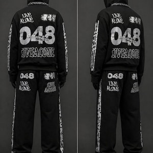 May include: Black hooded sweatshirt and matching sweatpants set. The back of the hoodie features the text "LIVE ALONE", "048", and "IVEALONE". The sweatpants also have the text "048 LIVE ALONE".