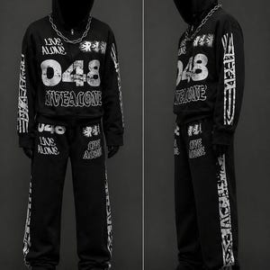 May include: Black hooded sweatshirt and matching sweatpants set with white graphic text and numbers. The text includes "LIVE ALONE" and "048". A silver chain necklace is worn with the hoodie. The outfit is completed with black sneakers.