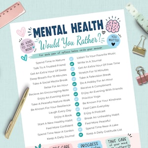 May include: A white paper sheet titled Mental Health Would You Rather with blue and pink text and illustrations. It lists pairs of self-care activities separated by or circles. A gold pen, a pink ruler, and two metal binder clips are visible.